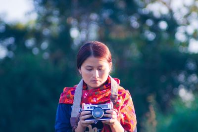 Young woman photographing while standing against trees