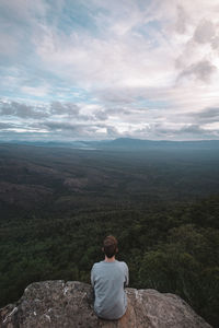 Rear view of man sitting on landscape against sky