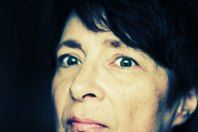 Close-up portrait of mature woman against black background