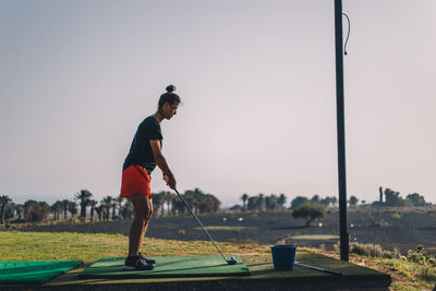 Full length of woman standing on golf course against clear sky