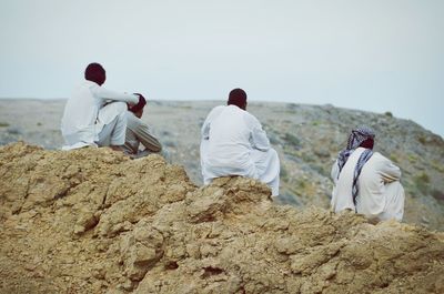 Rear view of men in traditional clothing sitting at rocky mountain