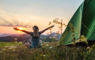 Rear view of woman standing on field against sky during sunset