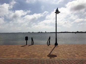Wooden posts on street by sea against sky