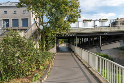 Footbridge over footpath amidst plants against sky