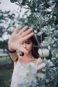 Portrait of beautiful young woman showing stop gesture while standing by plants