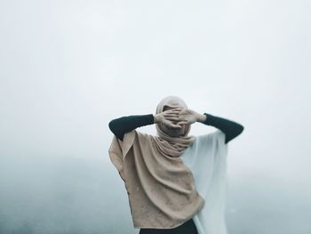 Young woman covering eyes while standing against sky during foggy weather