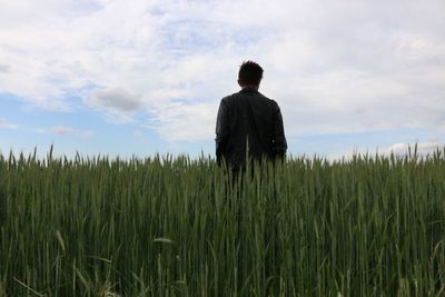 Rear view of girl standing on field against cloudy sky