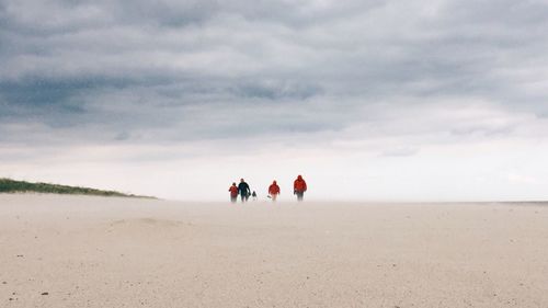 People walking at beach against cloudy sky