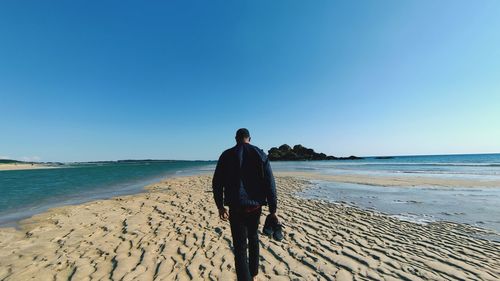 Rear view of man standing at beach against sky