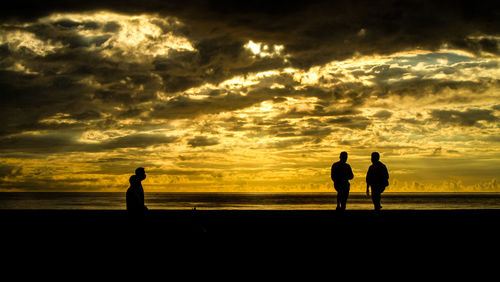 Silhouette men standing on beach against sky during sunset