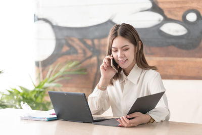 Young woman using mobile phone while sitting on table