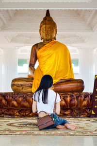 Rear view of young woman looking at giant buddha statue