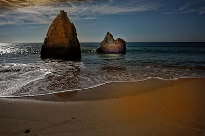 Rocks on beach by sea against sky