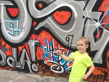 Portrait of boy standing against multi colored graffiti on wall