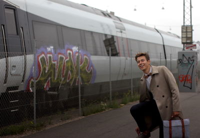 Young man standing by train at railroad station platform