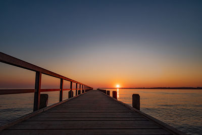 Pier over sea against clear sky during sunset