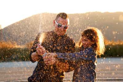 Father and son spraying soda in air at sunset