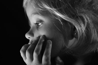 Close-up cute girl looking away against black background