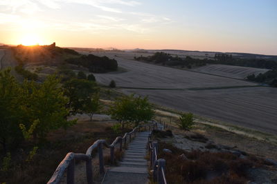 Footpath by landscape against sky during sunset