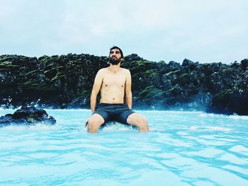 Shirtless man sitting in river