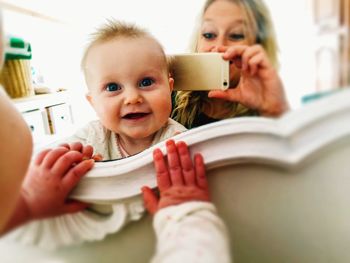 Portrait of cute baby with mother photographing in front of mirror