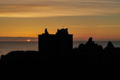 Silhouette buildings by sea against sky during sunset
