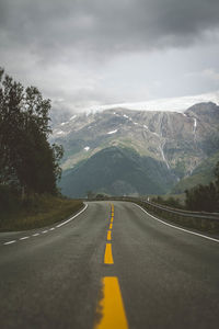 Road leading towards mountains against cloudy sky