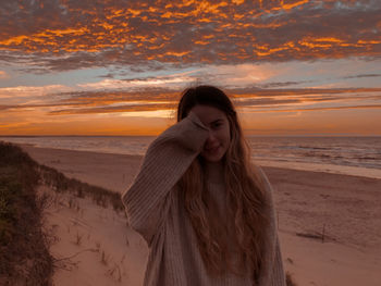 Young woman standing at beach during sunset