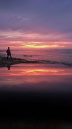 Low angle view of man standing at beach against sky during sunset