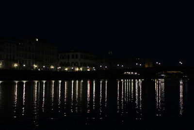 Illuminated buildings by river against sky at night