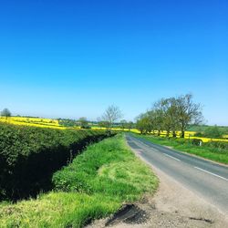 Road amidst field against clear blue sky