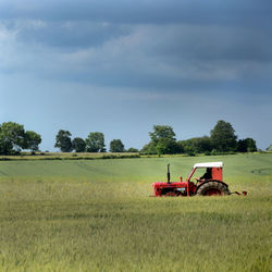 Farmer driving tractor on green field against sky