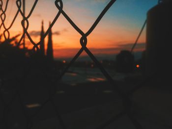 Close-up of silhouette chainlink fence against sky during sunset