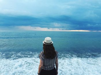 Rear view of woman wearing hat looking at sea against cloudy sky