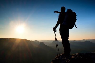 Sharp silhouette of a tall man on the top of the mountain with sun in the frame