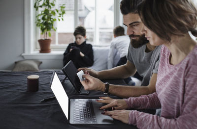 Man and woman shopping online with sons in living room at home