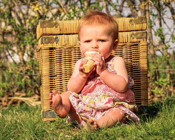 Portrait of cute baby girl eating ice cream while sitting on grassy field in park