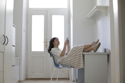 Woman using smart phone while sitting on chair at home