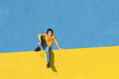 Young man looking away against yellow wall