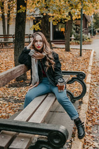 Portrait of young woman sitting on tree during autumn