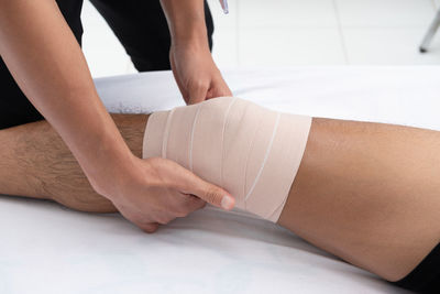 Close-up of healthcare worker wrapping bandage on man knee