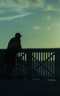 Silhouette man standing by railing against sky