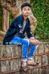 Portrait of young man sitting against brick wall