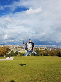 Portrait of young man jumping on grassy field against sky