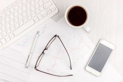Flat lay photo of white office desk with laptop, smartphone, eyeglasses, notebook and pen 