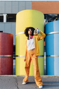 Young woman carrying boom box on shoulder in front of colorful pipes