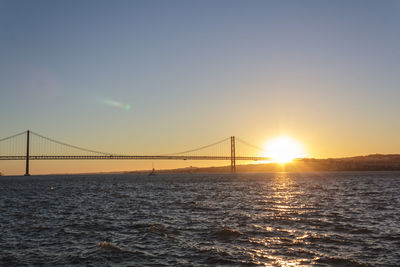 Suspension bridge over sea against sky during sunset