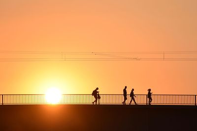Silhouette people walking on bridge against orange sky
