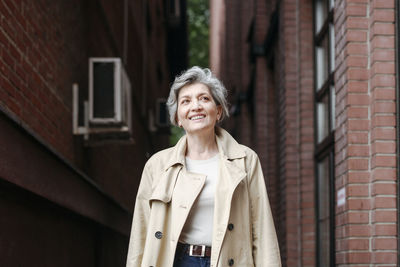 Portrait of a smiling young woman standing against building in city