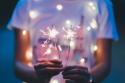 Midsection of person holding illuminated sparkler while standing outdoors at night